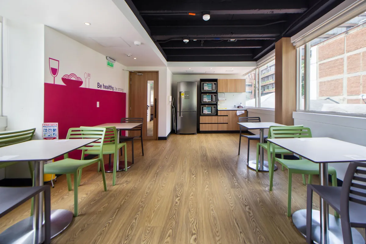 Office breakroom with tables, green chairs and a kitchen wall