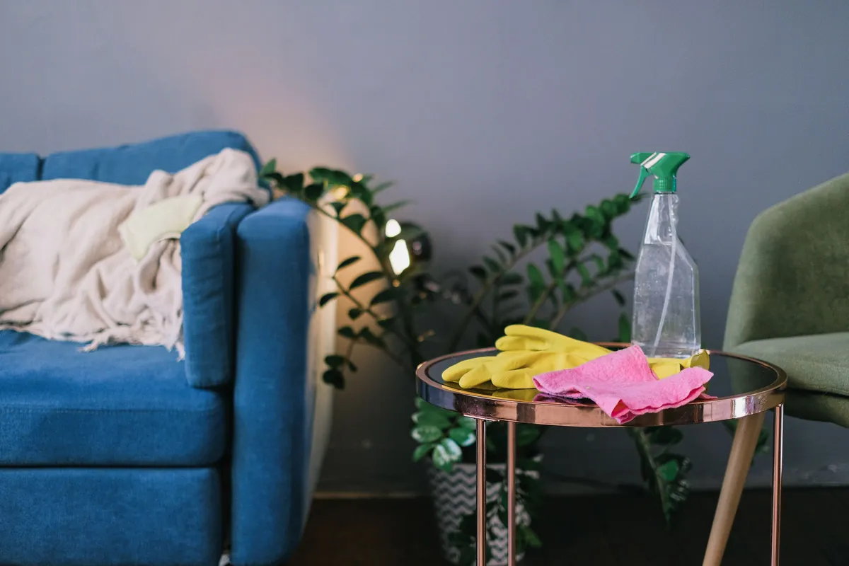 Spray bottle and gloves on a side table beside a blue sofa